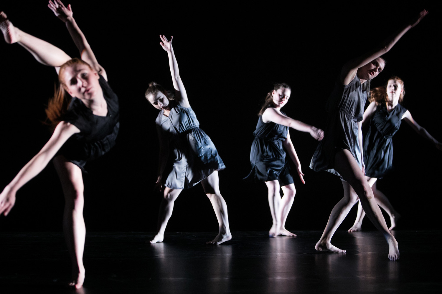 Five dancers in various movements dark costumes and lighting 