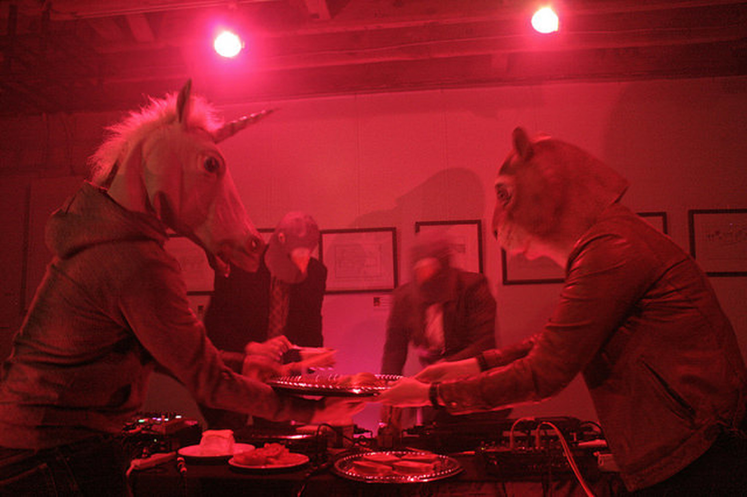 4 people in animal masks playing turn tables and passing food
